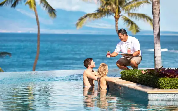 Server handing a couple at Four Seasons Resort Maui drinks to sip at the pool